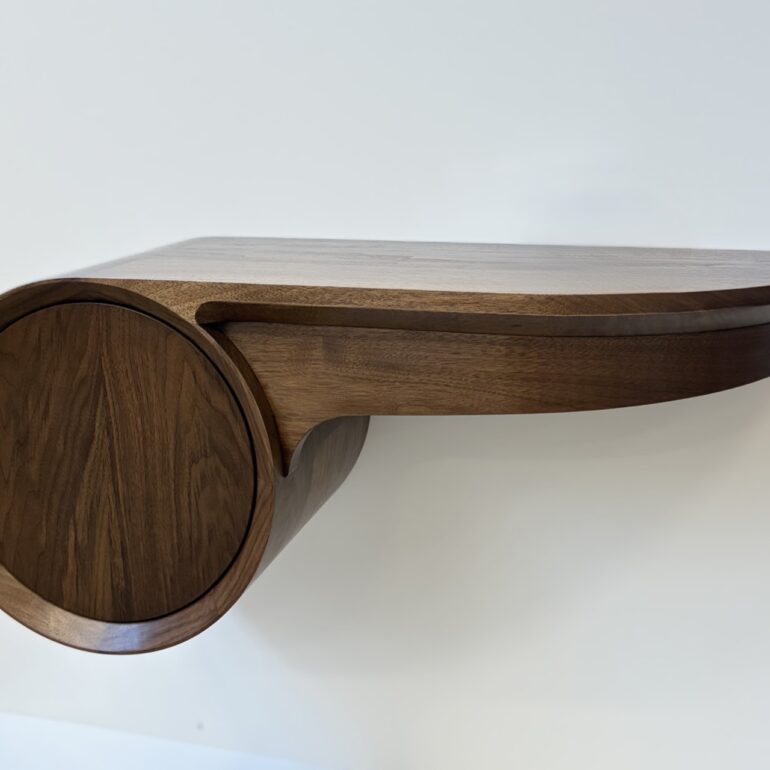 whistle shaped dark timber wall mounted shelf with a circular push-to-open drawer